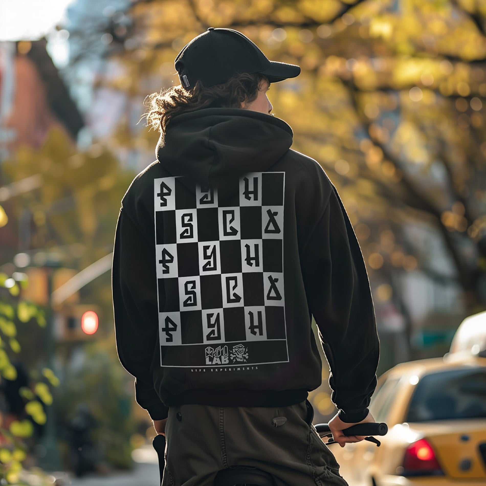 Junger Mann trägt den Hoodie Mindset von PsychoLab, zeigt das auffällige Schachbrettmuster mit 'PSYCHO' auf der Rückseite, ideal für urbanen Stil.